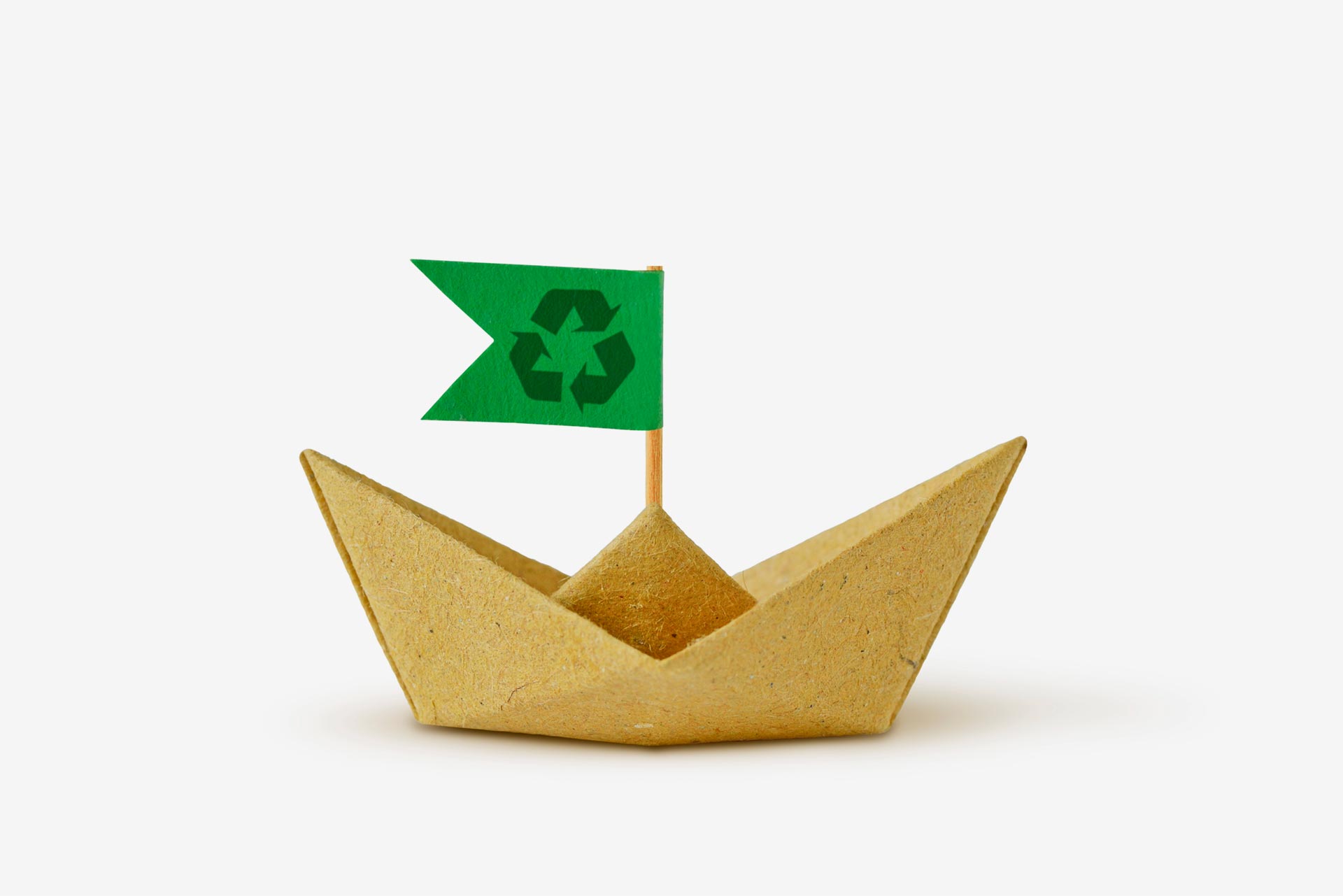 un origami de un barco hecho con papel reciclado y que lleva una bandera con el símbolo del reciclaje